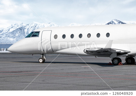 Close-up of the front of the luxury white corporate airplane at the winter airport on the background of high scenic snow capped mountains 126048920