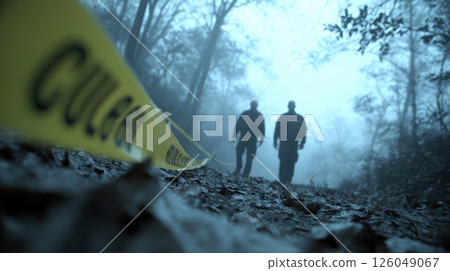 Silhouetted figures walk alongside yellow caution tape on foggy morning in eerie woodland setting, murder scene in misty forest 126049067