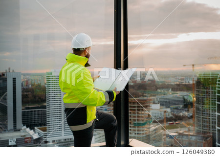 Engineer overseeing city construction project with blueprints in hand. Engineer overseeing city construction project with blueprints in hand. 126049380