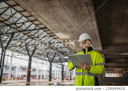 Female engineer checking building documentation on clipboard at construction site. Female engineer checking building documentation on clipboard at construction site. 126049420