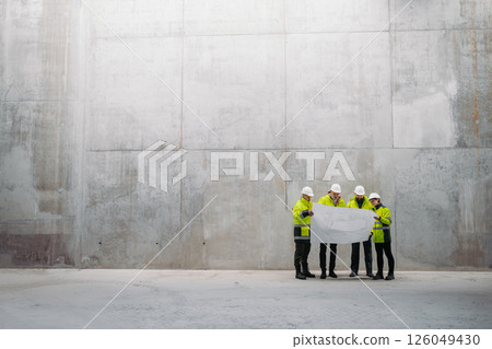 Team of engineers and construction workers reviewing blueprints, building site. 126049430