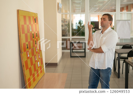 Caucasian man standing at wall mounted magnetic chessboard demonstration. Caucasian man standing at wall mounted magnetic chessboard demonstration. 126049553