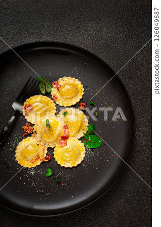 fresh ravioli, with butter, spices and herbs, fried bacon, on a black plate, top view, dark background, no people, 126049887