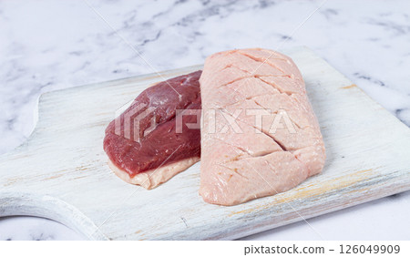 Fresh raw duck breasts, laid out on a wooden cutting board, on a white marble surface 126049909