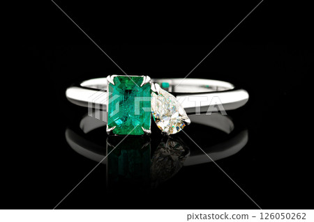 silver or gold ring with emerald stone and diamonds on black background 126050262
