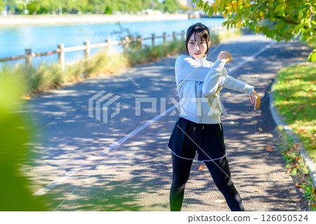 A cool woman stretching her shoulders and shoulder blades on a road in the sunlight, warm-up, exercise, trimming A cool woman stretching her shoulders and shoulder blades on a road in the sunlight, warm-up, exercise, trimming 126050524