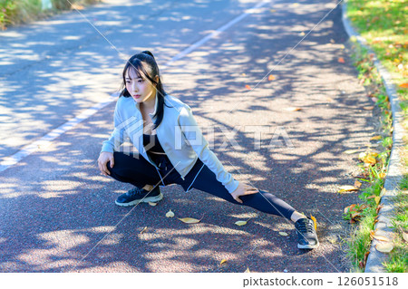 A cool woman stretching her legs on a sidewalk along the river, bending and stretching, dieting, walking, exercise 126051518