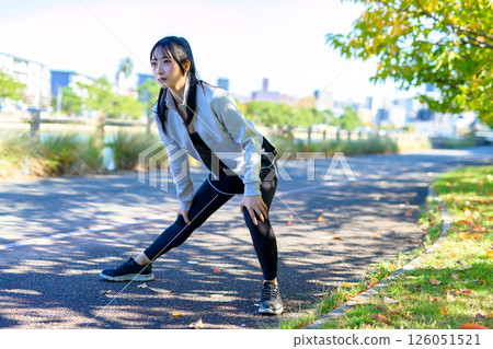 一位酷酷的女人在河邊的人行道上伸展雙腿，彎曲和伸展，節食，散步，鍛煉 126051521