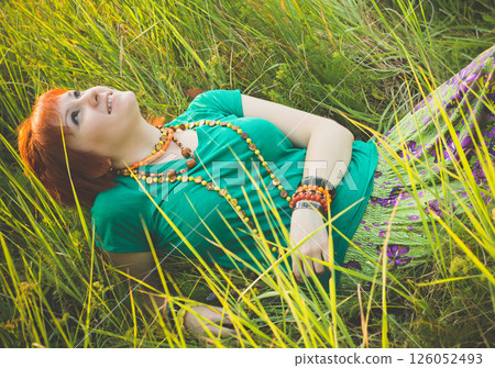 Young red-haired woman lying in the grass and enjoying a sunny summer day. Happy smiling young girl in nature. Young red-haired woman lying in the grass and enjoying a sunny summer day. Happy smiling young girl in nature. 126052493