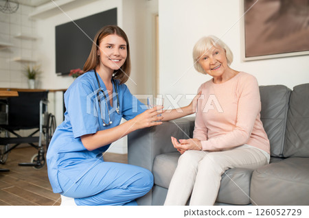 Nurse in uniform offering health support and nursing care to elderly patient in retirement home 126052729
