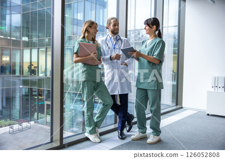 Group of young doctors in lab coats walking in the clinic corridor and talking 126052808