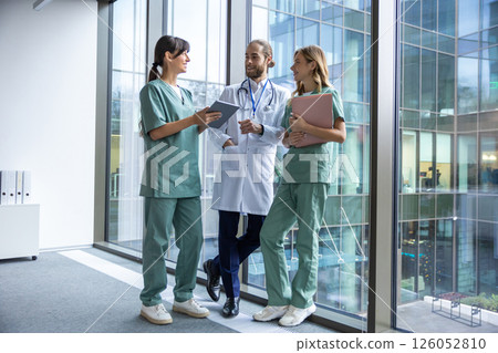 Group of young doctors in lab coats walking in the clinic corridor and talking Group of young doctors in lab coats walking in the clinic corridor and talking 126052810