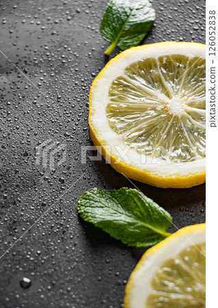 Fresh juicy lemon slices on a black background. Cocktail ingredient - mint leaves and lemon. Water drops on ripe lemon. Food background. Vertical photo. 126052838