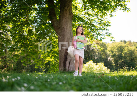 Child walking in park with backpack and bools in hands book on sunny day 126053235
