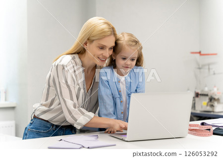 Mother tailoring a new model in her dress design studio, her daughter watching 126053292