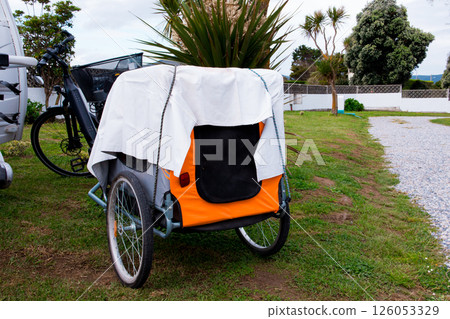 Orange pet trailer for bicycle with white cover in outdoor setting Orange pet trailer for bicycle with white cover in outdoor setting 126053329