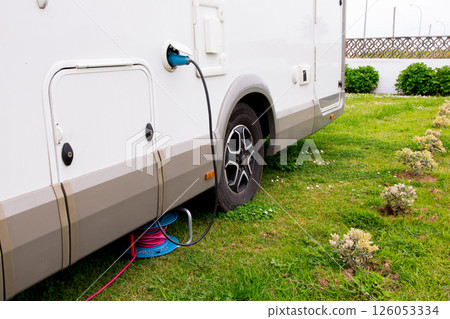 Camper van power connection on grass with electric cable reel for outdoor use Camper van power connection on grass with electric cable reel for outdoor use 126053334