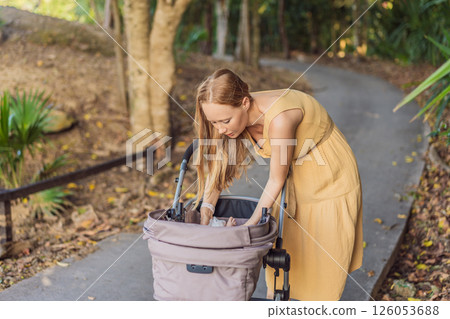 Mother changing her baby diaper in a stroller. Parenting, baby care, and motherhood on the go concept Mother changing her baby diaper in a stroller. Parenting, baby care, and motherhood on the go concept 126053688
