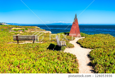 Rusty coastal pyramid sculpture and benches overlooking the Pacific Ocean in Santa Cruz, California, surrounded by lush ground cover and dramatic coastal cliffs under a bright blue sky Rusty coastal pyramid sculpture and benches overlooking the Pacific Ocean in Santa Cruz, California, surrounded by lush ground cover and dramatic coastal cliffs under a bright blue sky 126053936