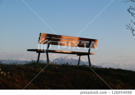 A wooden bench is sitting on a grassy hill overlooking a mountain A wooden bench is sitting on a grassy hill overlooking a mountain 126054099