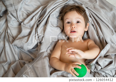 Top view of cute caucasian toddler playing ball in bed. Top view of cute caucasian toddler playing ball in bed. 126054412