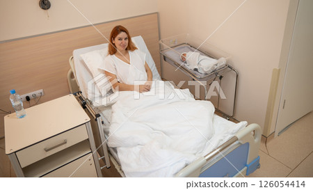 A young mother admires her newborn son in the maternity hospital. A young mother admires her newborn son in the maternity hospital. 126054414