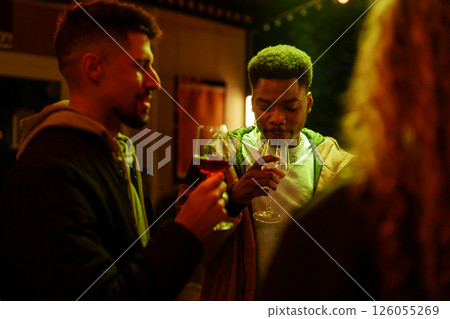 Friends enjoying conversation and drinks at a lively evening gathering under warm lights 126055269