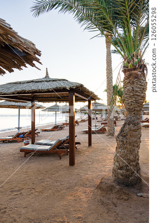 Peaceful beach setting with thatched umbrellas and lounge chairs at sunset 126055298
