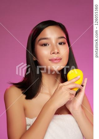 Young woman showcasing a yellow skincare device against a vibrant pink background 126055360