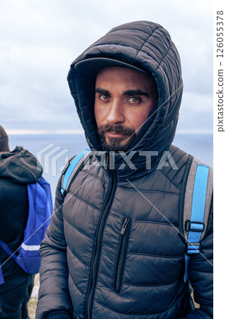 Man wearing a hooded jacket stands near a coastline on a cloudy day, ready for an adventure in nature Man wearing a hooded jacket stands near a coastline on a cloudy day, ready for an adventure in nature 126055378