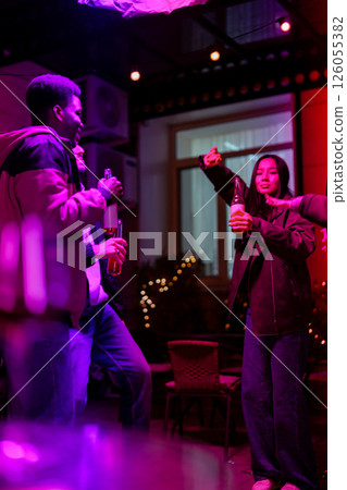 Friends enjoying drinks and dancing in a lively atmosphere at night in a vibrant venue 126055382