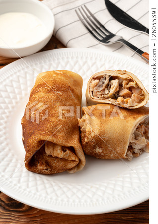 Delicious rolled pancakes filled with savory chicken served on a white plate beside a small bowl of yogurt 126055391