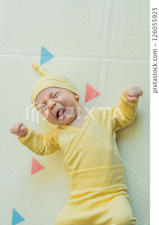 Adorable baby in a yellow hat lying on a play mat. Cozy newborn moment with soft textures and bright colors. Infant development, sensory play, and early childhood concept 126055925