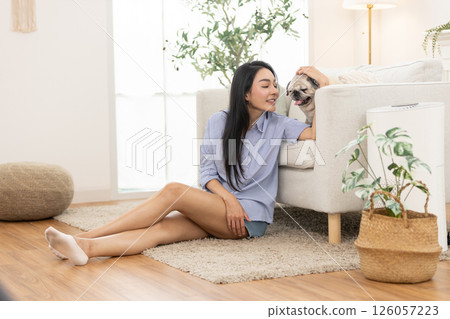 A woman enjoys quality time with her pug, sharing smiles and affection in a comfortable living room. The atmosphere is warm and relaxed, perfect for bonding with pets. 126057223