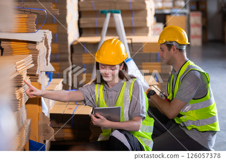 Operational or general worker man and women yellow hardhat using check quality and stock cardboard product. Large industry in paper production line warehouse. 126057378