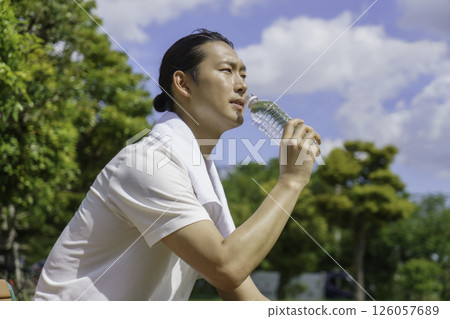 一位年輕人坐在公園長椅上補充水分 126057689