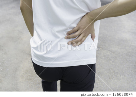 A young man's feet holding his lower back because his lower back hurts while running Lower back pain 126058074