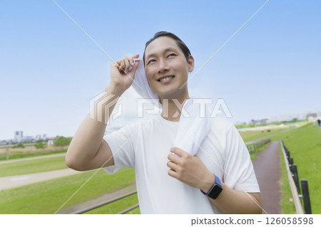 Young man wiping sweat with a towel while running Young man wiping sweat with a towel while running 126058598