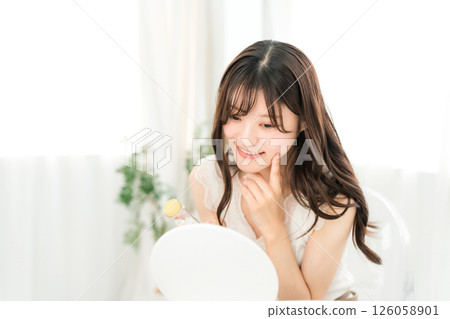 Smiling Asian woman holding a bottle of medicine/supplements and looking in the mirror 126058901
