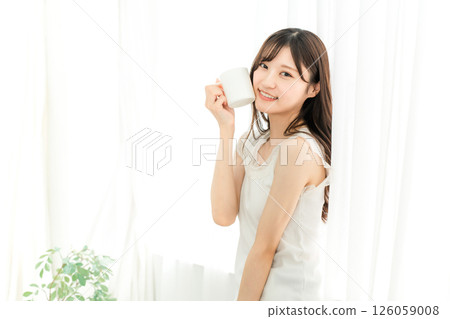 Smiling Asian woman drinking hot water, coffee, hot drink, cafe au lait, cafe latte at home in the morning 126059008