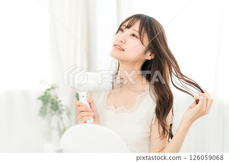 A woman blow-drying her hair with a hair dryer (hair care) 126059068