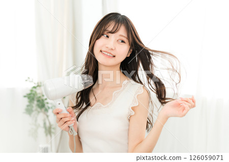 A woman blow-drying her hair with a hair dryer (hair care) A woman blow-drying her hair with a hair dryer (hair care) 126059071