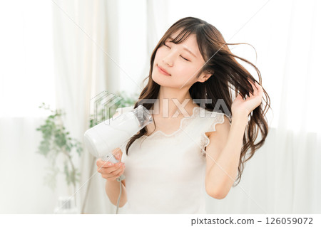 A woman blow-drying her hair with a hair dryer (hair care) 126059072