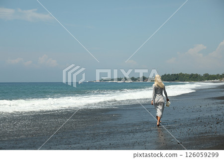 Young woman walking on black sand beach, space for text 126059299