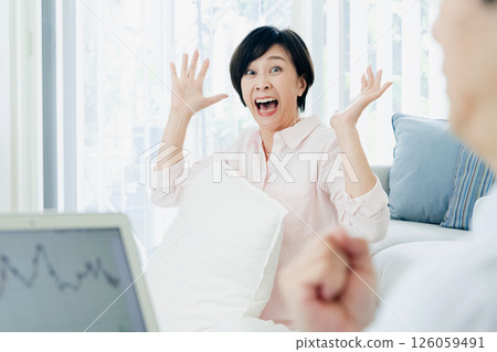 A middle-aged couple happily watching a computer in the living room A middle-aged couple happily watching a computer in the living room 126059491
