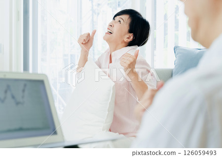 A middle-aged couple happily watching a computer in the living room A middle-aged couple happily watching a computer in the living room 126059493