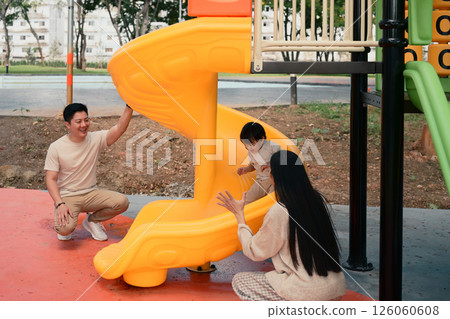 Happy parents playing with their young child at the playground slide on a sunny day. 126060608
