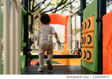 Back view of toddler enjoying playtime at a colorful outdoor playground 126060617