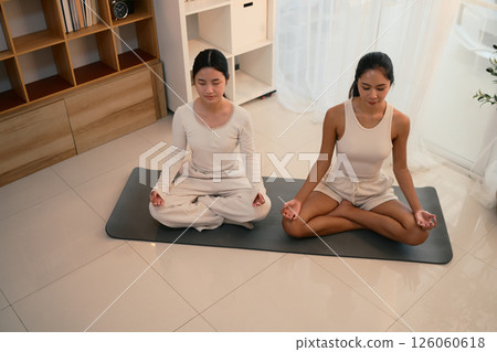 Calm and focused mother and daughter practicing yoga together in a peaceful indoor 126060618