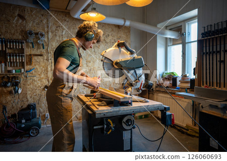 Skilled carpenter use miter saw, measure and trim wood beams in workshop. Handyman precision cut 126060693